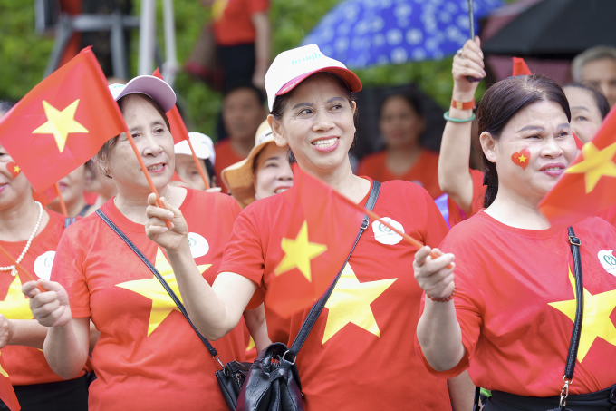 Người cao tuổi mặc áo cờ đỏ sao vàng, tham dự hoạt động hát Quốc ca dù trời mưa.